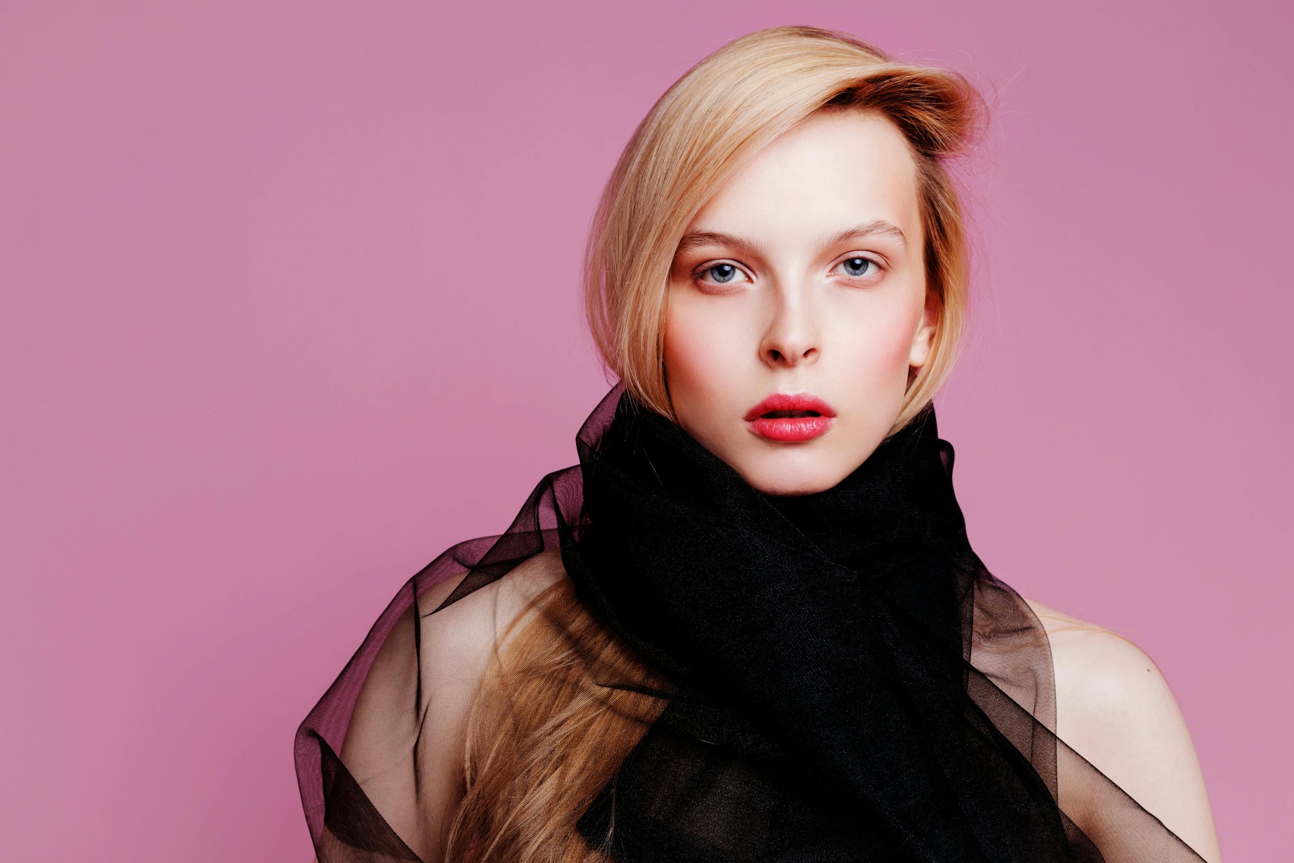 Striking portrait of a woman with blonde hair and red lips against a pink background.